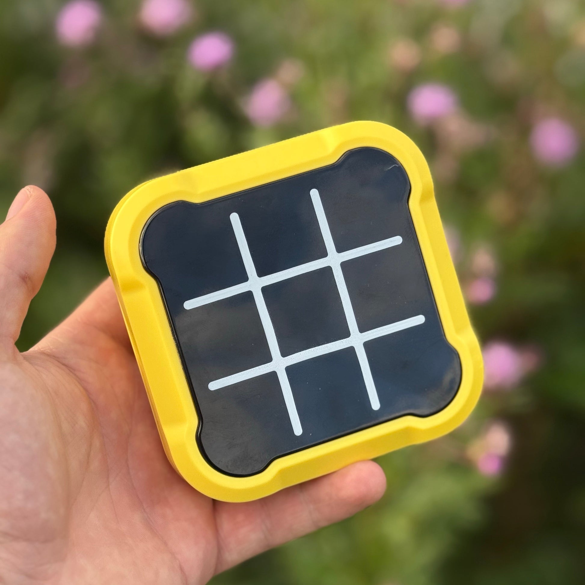 Hand holding a small solar panel with tic-tac-toe grid against a blurred natural background